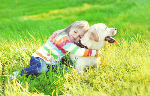 Happy child hugging labrador retriever dog on grass in summer © rohappy