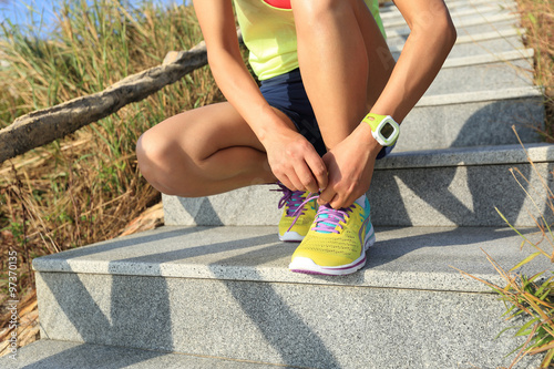 young woman runner tying shoelaces on stone trail