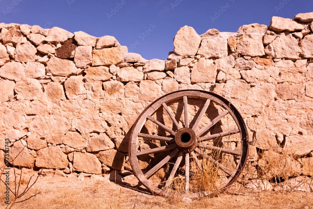 Old cart whee leans on broken stone walll