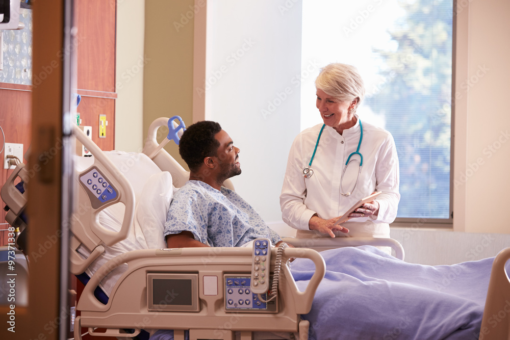 Hospital Doctor With Digital Tablet Talks To Male Patient Hospital Doctor With Digital Tablet Talks To Male Patient