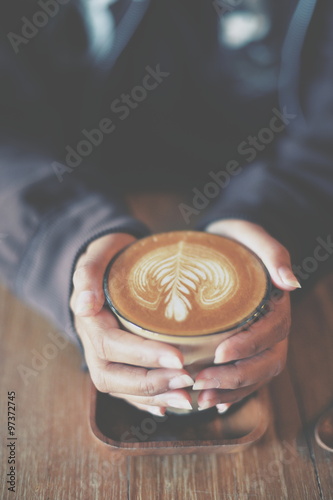 Woman hand hold cup of coffee latte on the wood texture   in vintage color tone photo