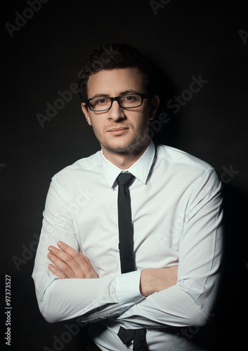 Confident businessman. Confident young man keeping his arms crossed and looking at camera