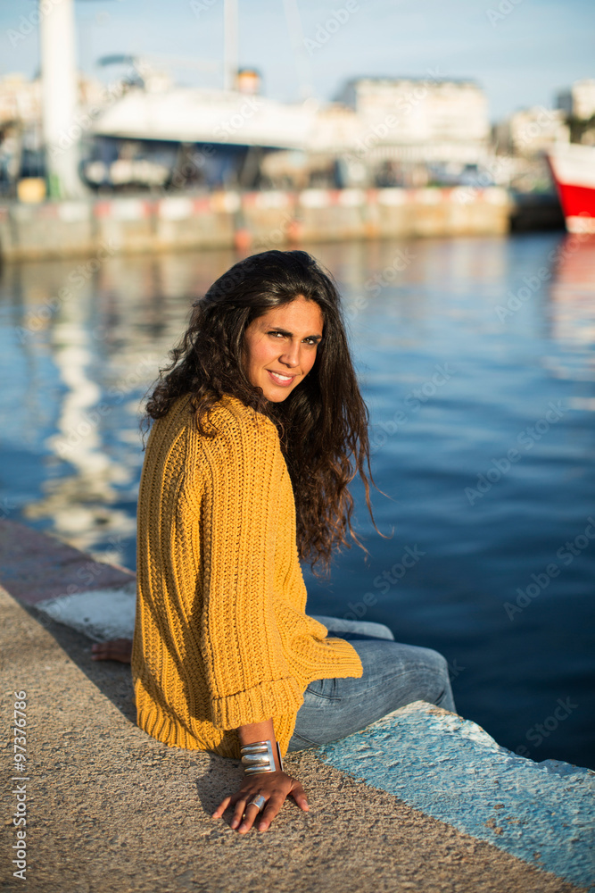 Portrait of smiling young woman sitting on pier and looking at camera