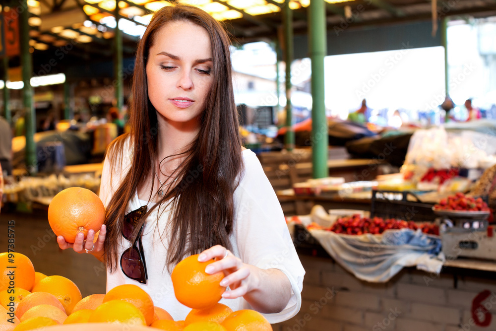 Young girl, wearing on white t-shirt, is choosing oranges, on shopping