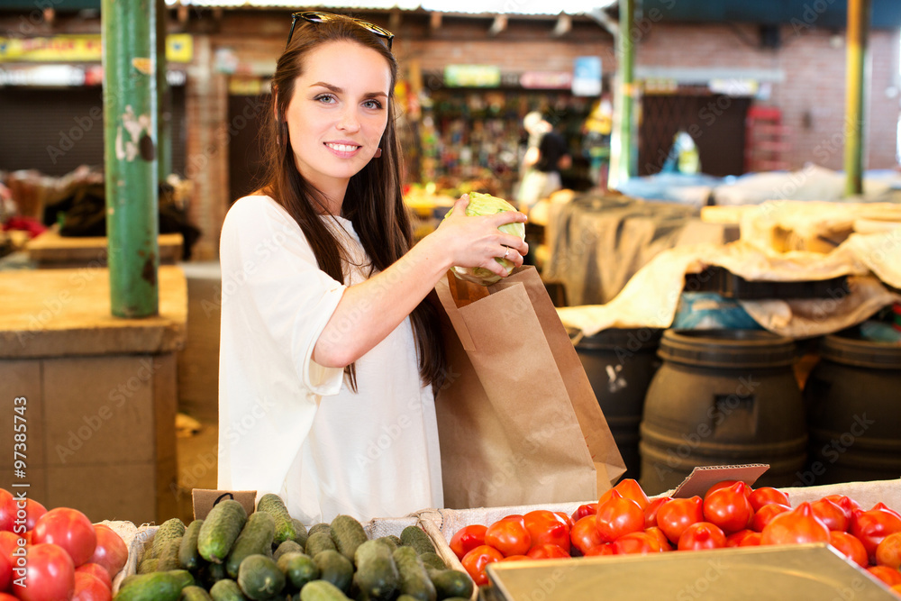 Smiling girl, wearing on white t-shirt, is putting cabbage to the paper bag