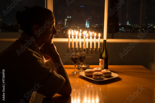 Girl sits by candles on Hanukkah holiday. Hanukkah celebration attributes. Judaic holiday of lights.