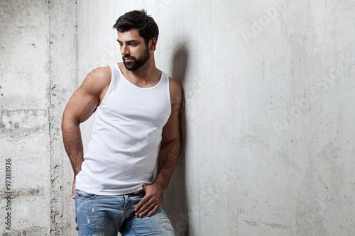 Brutal man in a white T-shirt and jeans standing on the cement wall background © deniskomarov