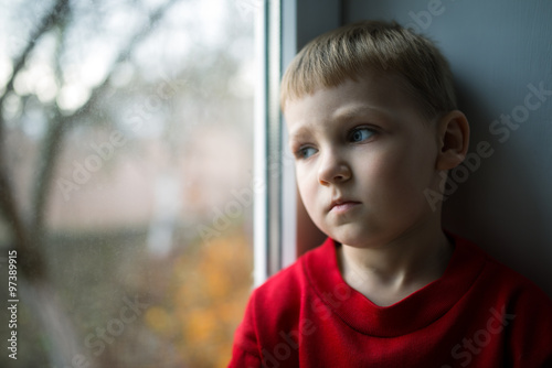 small boy sitting near window and thnking about something