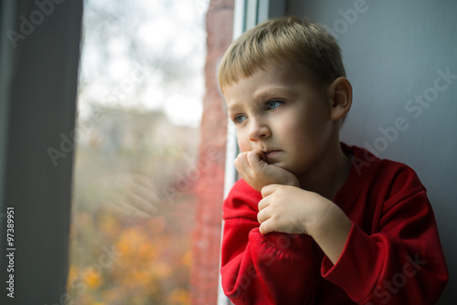 small boy sitting near window and thnking about something