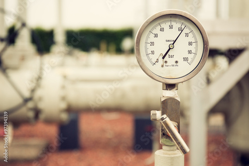 Closeup of a high pressure manometer, measuring natural gas pressure. Pipes and valves in the background. Selective focus photo