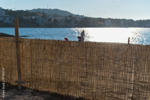 Beach with reed mat fence for sand protection during stormy weather. Playing and walking people on coastline on sunny day in winter photo