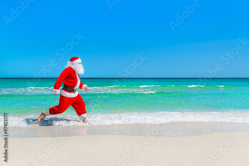 Christmas Santa Claus running at tropical beach on waves splashe