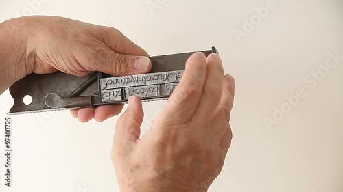 A man makes adjustments to blocks of metal type in his composing stick tool.