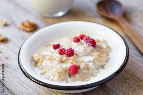 Oatmeal porridge with raspberries and milk on textured wooden table, country style healthy breakfast, Selective focus