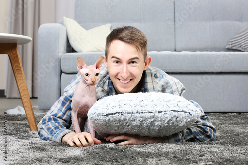 Young handsome man lies with cat on floor at home