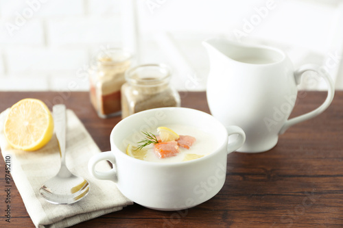 Delicious salmon cream soup on wooden table, which served with sliced lemon and spices