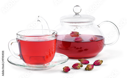 Fresh brewed rose tea in a glass teapot and a cup and a few buds of a tea rose isolated on white background.