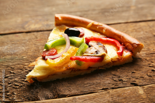 A slice of delicious pizza with vegetables, on wooden table