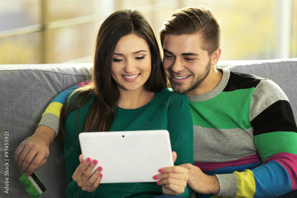 Young happy couple using credit card with tablet at home on light background Young happy couple using credit card with tablet at home on light background