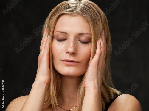 Beautiful blonde woman closed her eyes and pressed her hands to ears on a dark background.