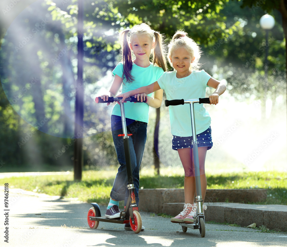 Fototapeta premium Small girls riding on scooters in park