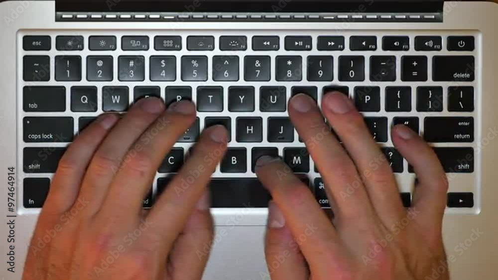 An overhead shot of a man typing on a laptop's keyboard.  	