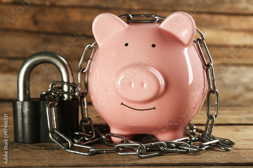 Piggy bank and chains on wooden background