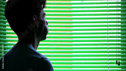Sad man worried in front of a venetian blind, talking at smartphone