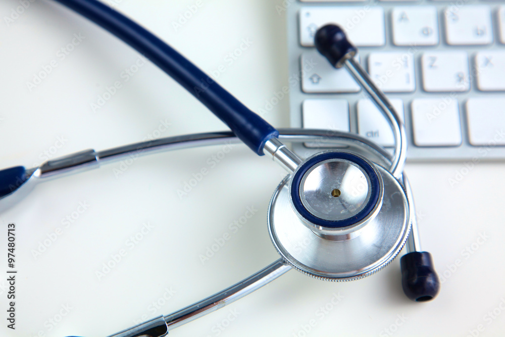 A medical stethoscope near a laptop on a wooden table, on white A medical stethoscope near a laptop on a wooden table, on white