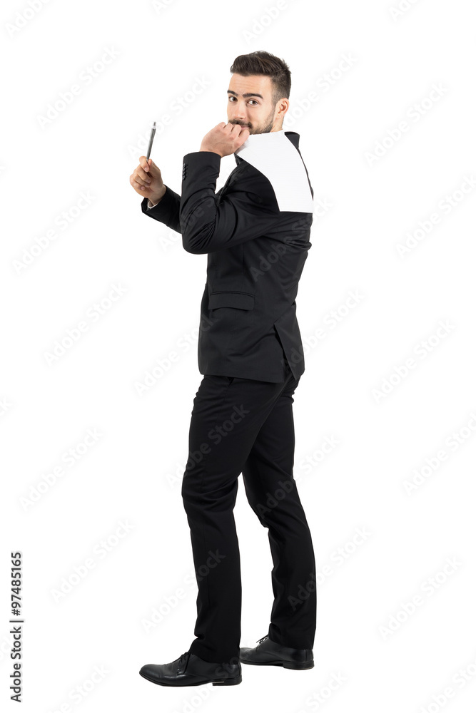 Young business man in suit holding contract paper on his back offering pen for signature. Full body length portrait isolated over white studio background. Young business man in suit holding contract paper on his back offering pen for signature. Full body length portrait isolated over white studio background.