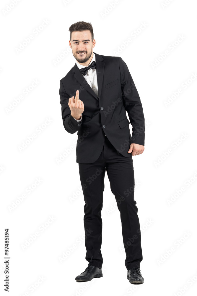 Rude young man in tuxedo with bow tie showing middle finger gesture at camera. Full body length portrait isolated over white studio background. Rude young man in tuxedo with bow tie showing middle finger gesture at camera. Full body length portrait isolated over white studio background.