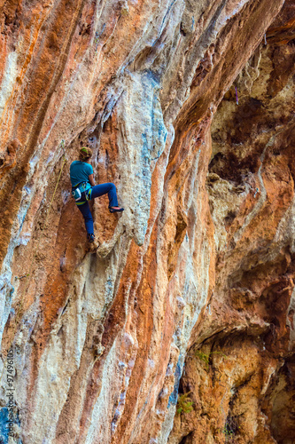 Young Rock Climber ascending steep colorful rocky Wall Lead Climbing