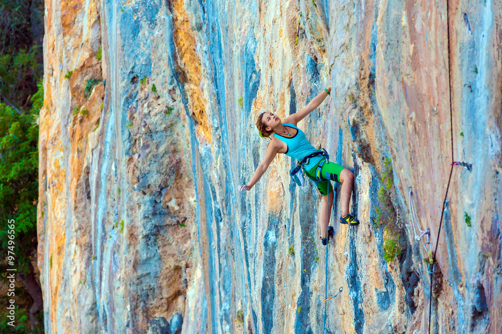 Obraz premium Young Female Climber ascending vertical rocky wall