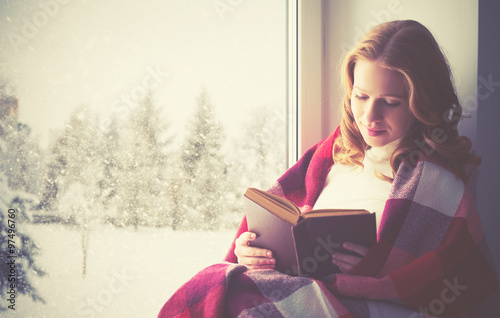 happy girl reading book by the window in winter photo