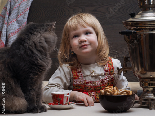 Девочка у самовара, в деревне. На столе сидит кот. Миска с баранками. Чашка с чаем. Самовар. Вкусный чай. Девочка одета в сарафан - национальная русская одежда