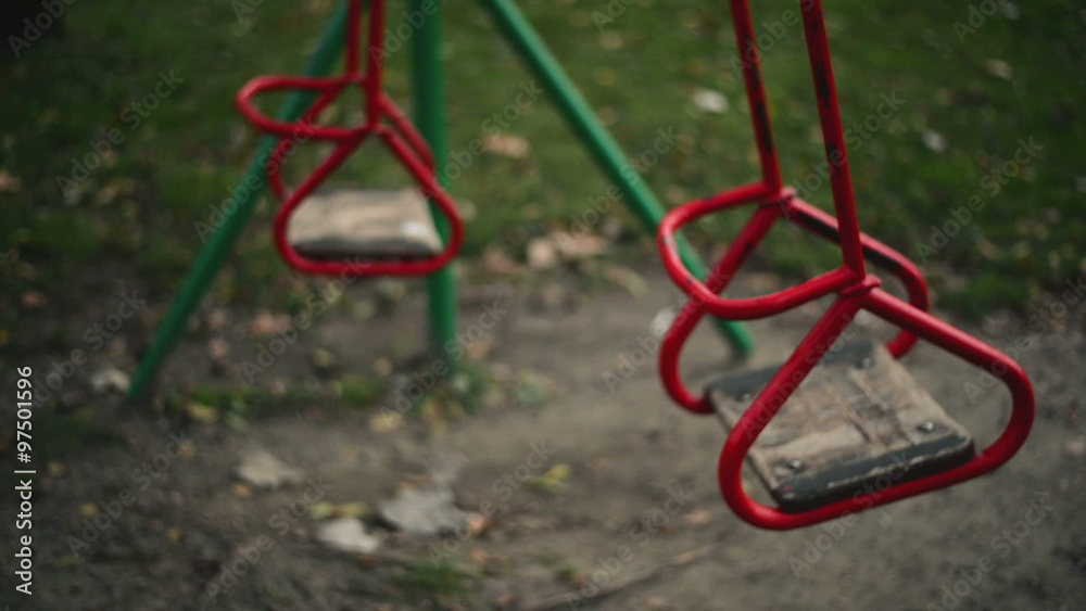 Empty red swing seat swaying in park playground on autumn afternoon Empty red swing seat swaying in park playground on autumn afternoon