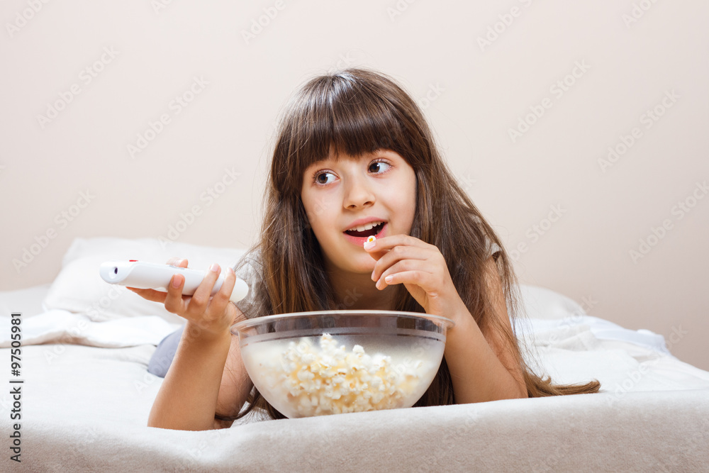 Little girl is watching tv and eating popcorn in her bed. Little girl is watching tv and eating popcorn in her bed.
