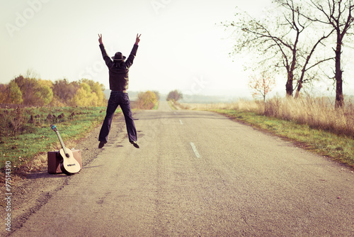 Photography Backview of guitar player in hat jumping on countryside road