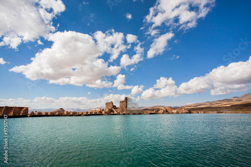 Blue water of a mountain lake under the heavy white clouds with the ruins of an ancient stone city