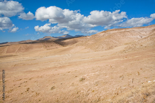 White clouds float over the arid landscape in a valley with a dried soil