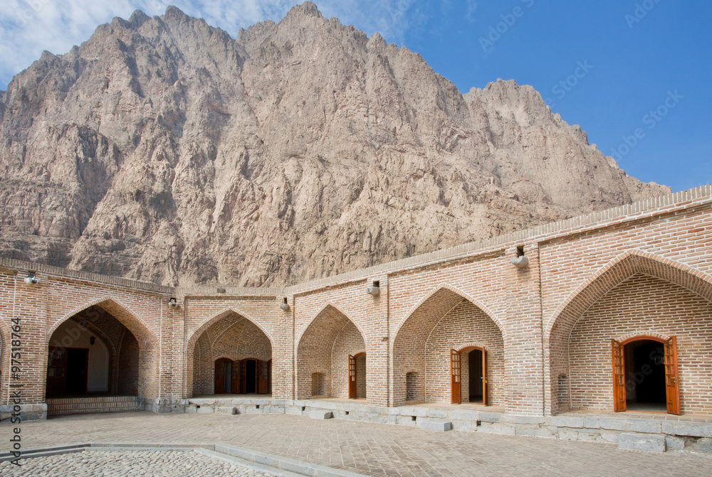 Fototapeta premium Mountain behind the historical brick walls of persian caravanserai with wide empty courtyard under the sun
