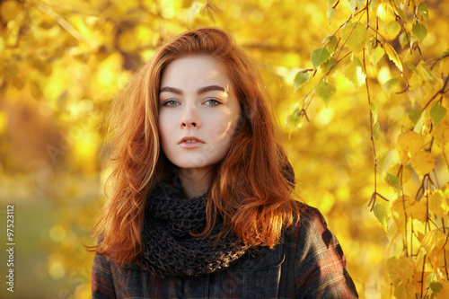 Art portrait of young beautiful redhead woman  in scarf and plaid jacket with autumn foliage background outdoors