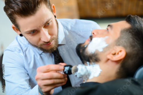 Professional barber shaving the beard of his client 