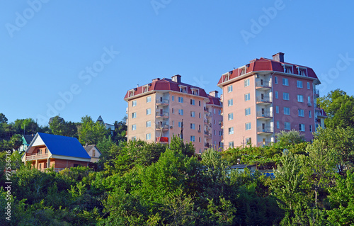 Многоэтажные жилые дома и одноэтажный деревенский дом на склоне невысокой горы в небольшом южном городе
