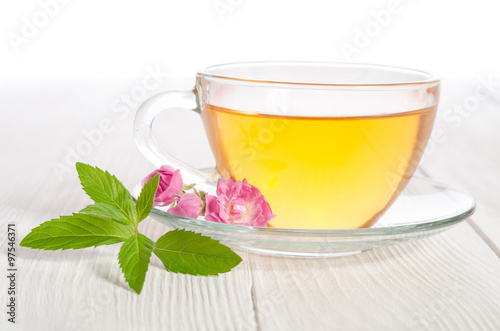 Glass cup of tea with mint and rose on white wooden table
