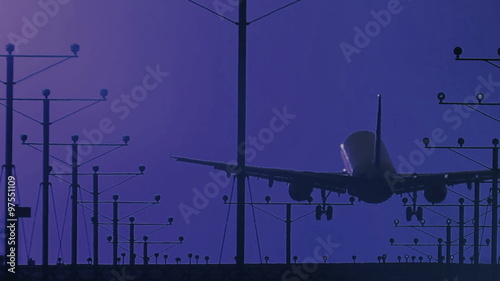 HD footage of a twin engine jet plane landing off center in silhouette against an dark blue night sky.