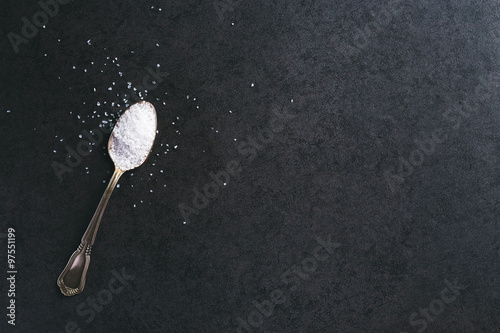 Silver spoon with salt on the table.