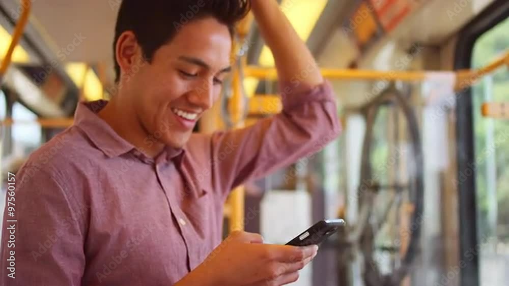A young man standing on a bus and using his phone