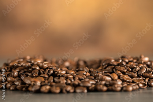 Kaffeebohnen liegen verteilt auf einem Tisch. Hintergrund orange-braun