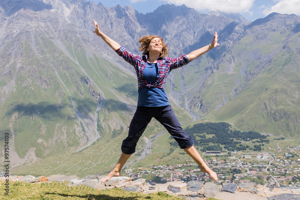Young woman jumping with hands up against the sky and mountain